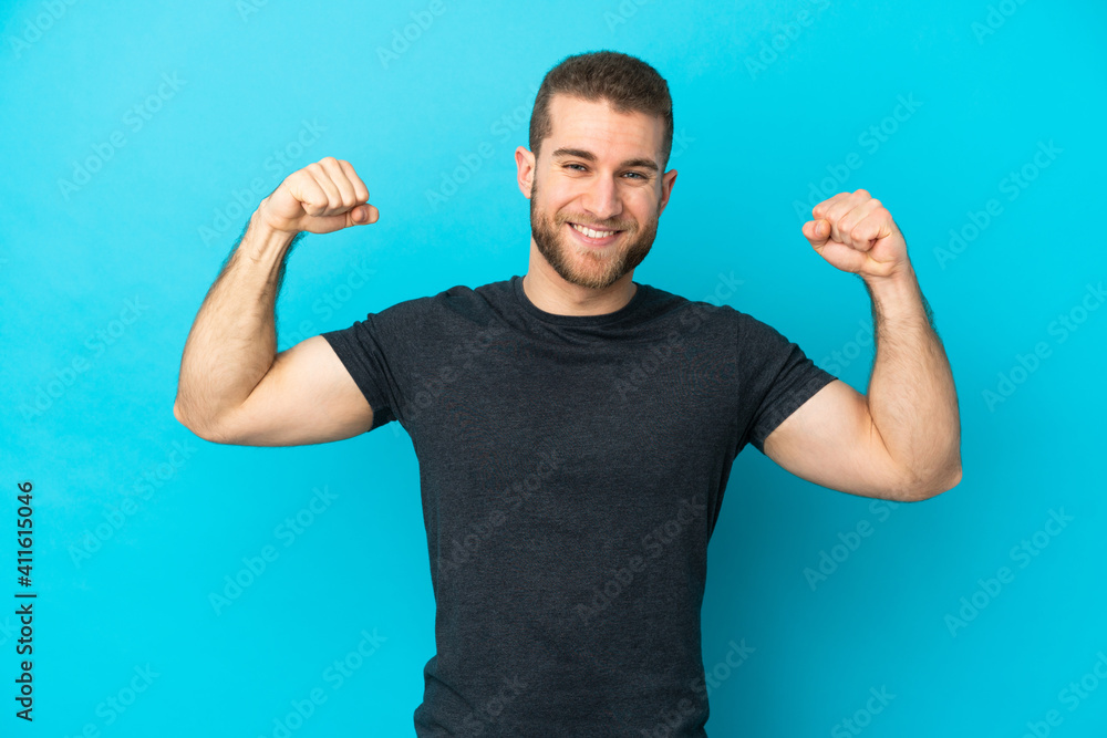 Young handsome caucasian man isolated on blue background doing strong gesture Young handsome caucasian man isolated on blue background doing strong gesture
