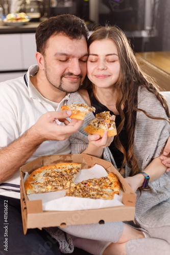 Happy couple at home feeding each other with pizza, dating at home. Care and love concept.