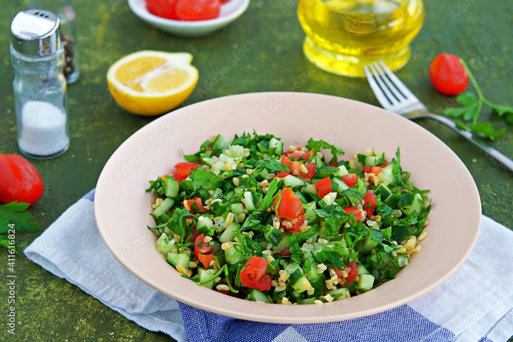 Tabbouleh, parsley, tomato and cucumber vegetable salad with bulgur in a clay plate on an olive concrete background. Salad recipes. Healthly food. Tabbouleh, parsley, tomato and cucumber vegetable salad with bulgur in a clay plate on an olive concrete background. Salad recipes. Healthly food.