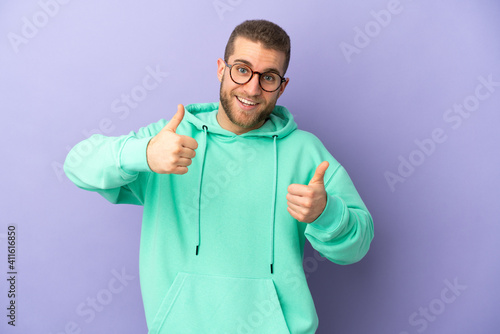 Young handsome caucasian man isolated on purple background giving a thumbs up gesture © luismolinero