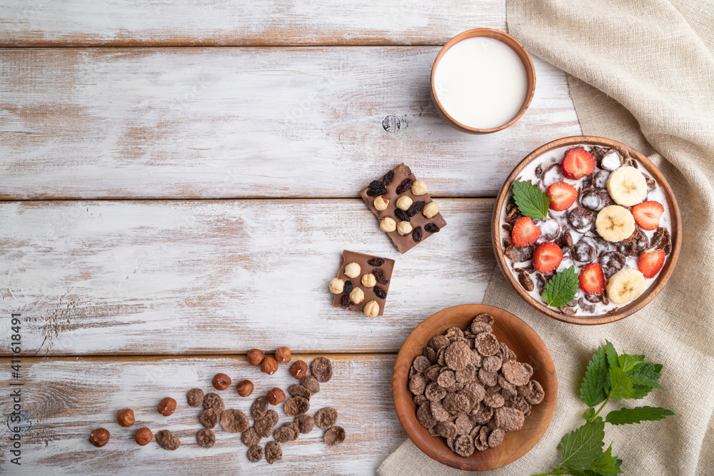 Chocolate cornflakes with milk and strawberry in wooden bowl on white wooden background. Top view, copy space. Chocolate cornflakes with milk and strawberry in wooden bowl on white wooden background. Top view, copy space.