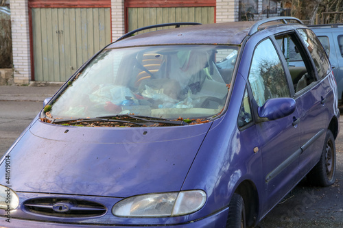 The detail of an abandoned broken car, now a wreck with damaged or broken windows and full of rubbish or waste. Occupies a parking place for the others. 