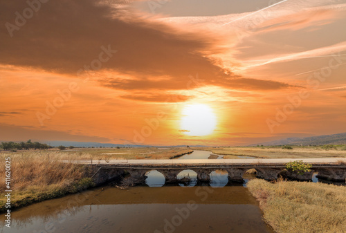 Old stone bridge over a river during sunset. The bridge is called 