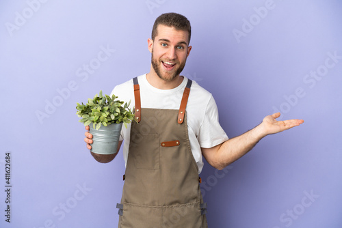 Gardener caucasian man holding a plant isolated on yellow background with shocked facial expression