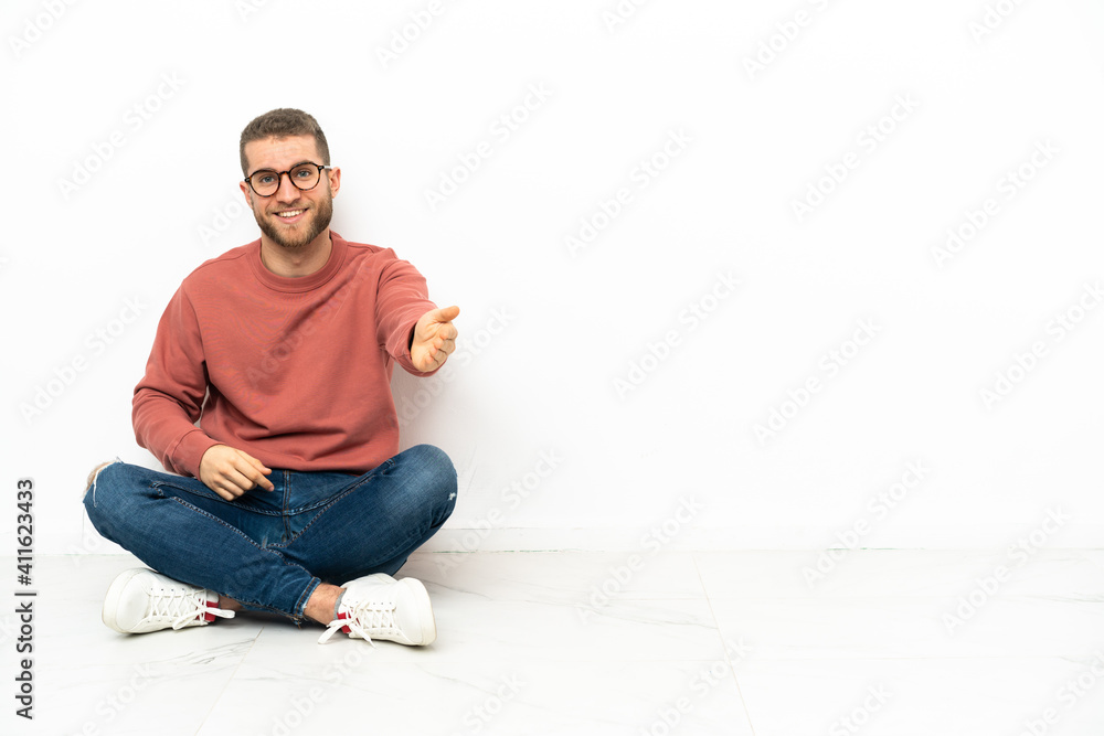 Young handsome man sitting on the floor shaking hands for closing a good deal Young handsome man sitting on the floor shaking hands for closing a good deal