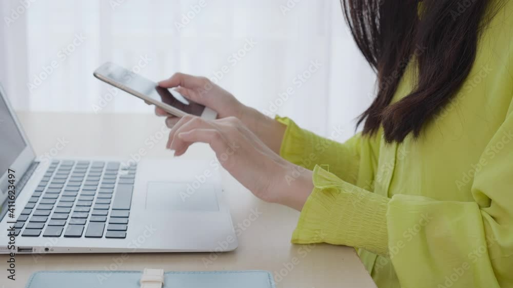 Closeup hand of young asian businesswoman working on laptop computer on desk at home office, freelance woman looking message on smart phone and typing on notebook, business and communication concept. Closeup hand of young asian businesswoman working on laptop computer on desk at home office, freelance woman looking message on smart phone and typing on notebook, business and communication concept.