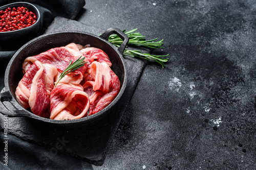 Raw bacon, strips of marbled meat in a pan. Black background. Top view. Copy space