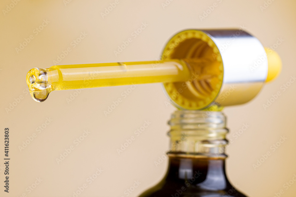 Cosmetic bottle and pipette with a drop of cosmetic oil and serum on light background macro image. Selective pocus closes up. Cosmetic bottle and pipette with a drop of cosmetic oil and serum on light background macro image. Selective pocus closes up.