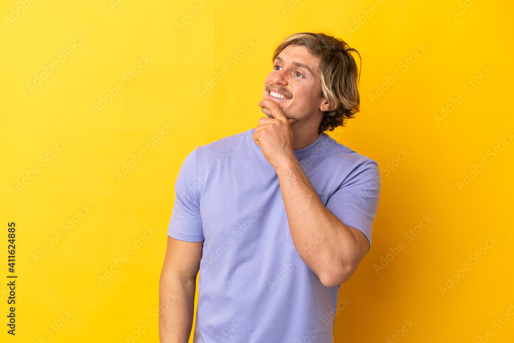 Handsome blonde man isolated on yellow background looking to the side and smiling Handsome blonde man isolated on yellow background looking to the side and smiling
