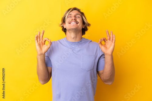 Handsome blonde man isolated on yellow background in zen pose