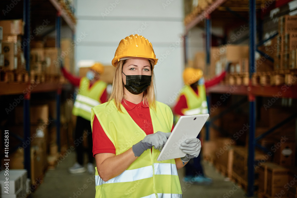 Portrait of happy female worker looking at camera inside warehouse while wearing face mask - Focus on face Portrait of happy female worker looking at camera inside warehouse while wearing face mask - Focus on face