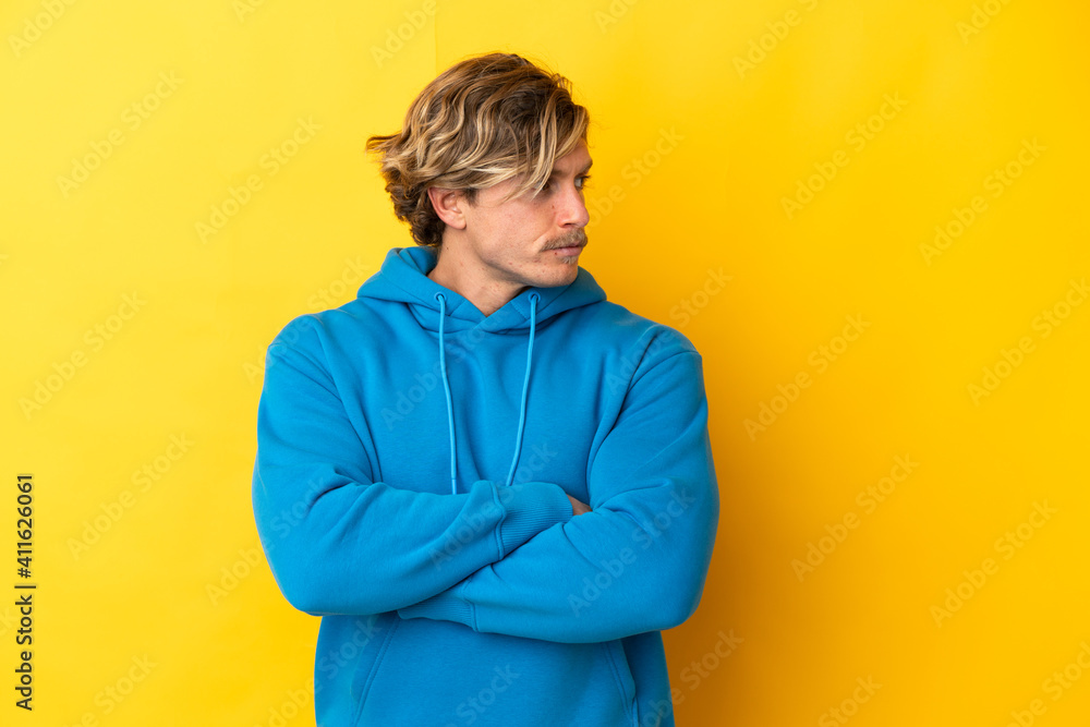 Handsome blonde man isolated on yellow background keeping the arms crossed Handsome blonde man isolated on yellow background keeping the arms crossed