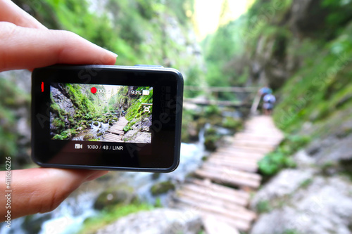 Hand holding small outdoor camera, filming (photographing) or taking pictures of tourists on wooden walk path in Prosiecka Valley (dolina) in Slovakia, Europe. A view through viewfinder of a camera. photo