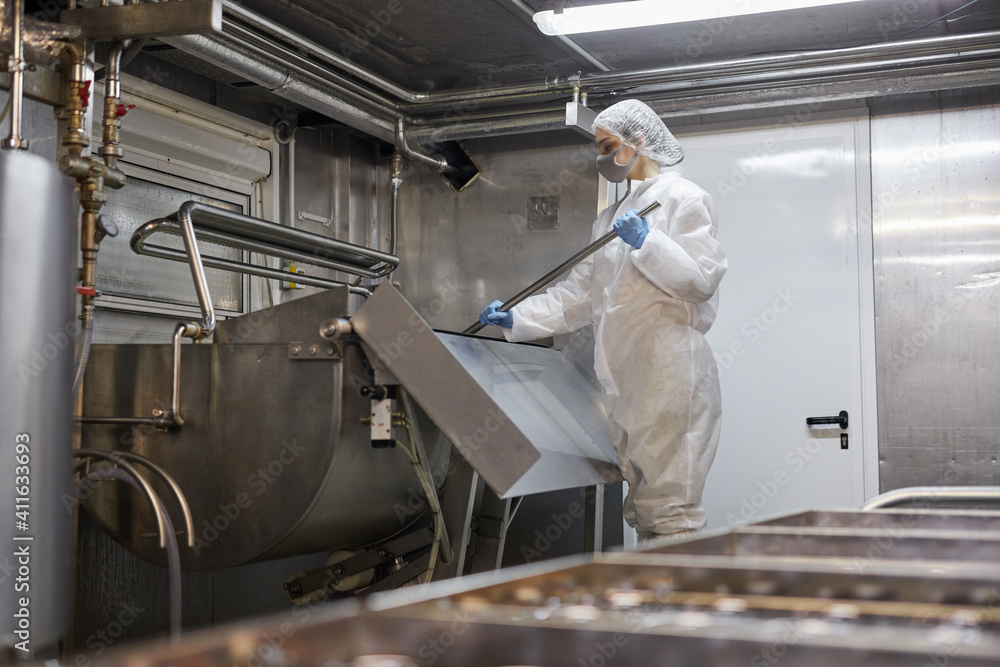 Wide angle portrait of young female worker mixing product at cheese and dairy factory, copy space