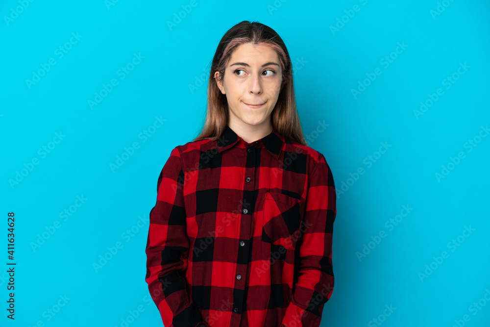 Fototapeta premium Young caucasian woman isolated on blue background having doubts while looking up
