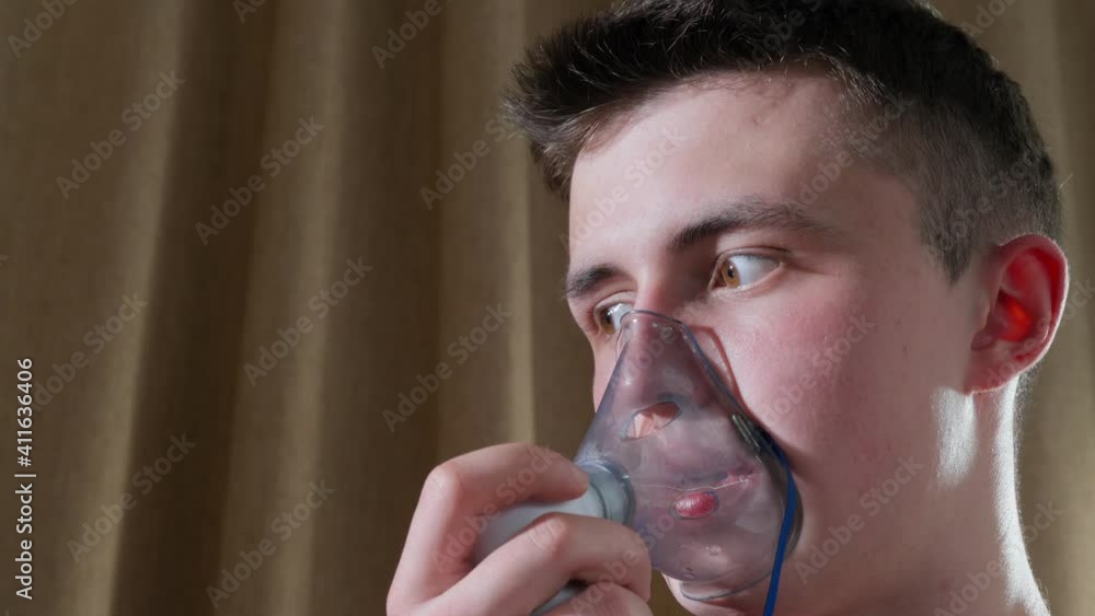 Teenage boy breathes in an oxygen mask. Inhalation of the respiratory tract. Mask inhaler. boy In A Mask For Breathing Inhalation Medication Teenage boy breathes in an oxygen mask. Inhalation of the respiratory tract. Mask inhaler. boy In A Mask For Breathing Inhalation Medication