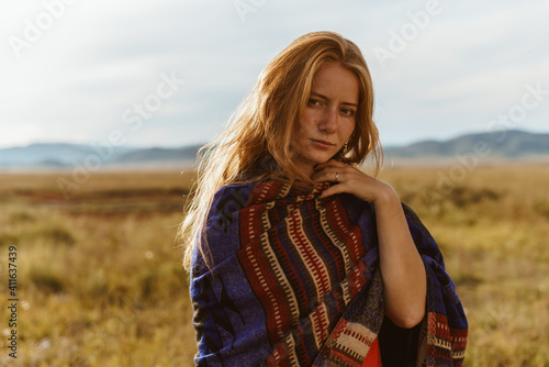 A brooding red-haired girl in ethnic clothing against the sunset in the steppes. Siberian witch, shaman. High quality photo