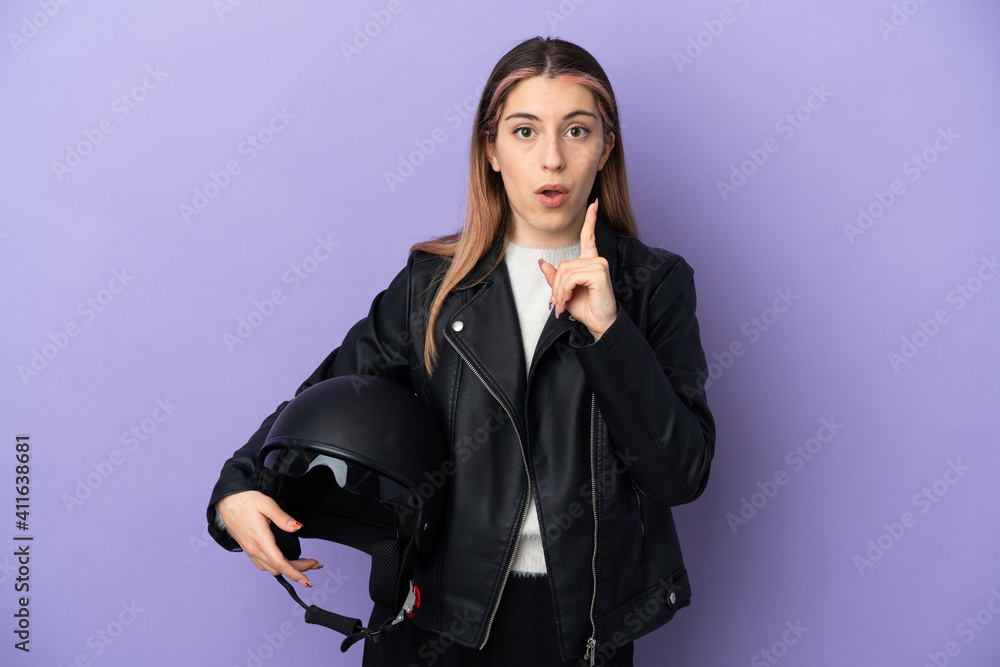 Young caucasian woman holding a motorcycle helmet isolated on purple background intending to realizes the solution while lifting a finger up Young caucasian woman holding a motorcycle helmet isolated on purple background intending to realizes the solution while lifting a finger up