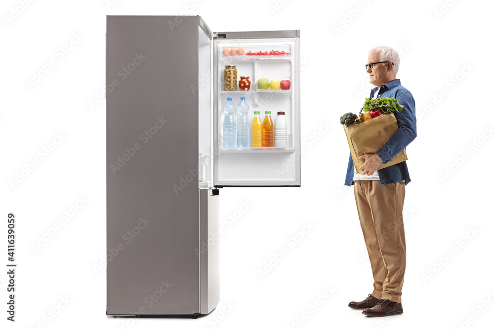 Mature man with a grocery bag looking at an open fridge Mature man with a grocery bag looking at an open fridge