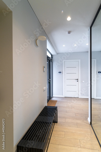 Interior of a spacious bright hallway in a new modern house. Comfortable black bench on one side of the corridor  in front of a sliding door closet with a large mirror