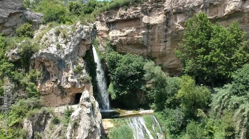 Aerial views of a waterfall with a cave and an old building in Catalonia, Spain