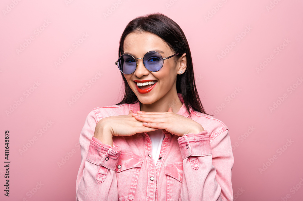 Portrait of beautiful happy fashionable caucasian girl in sunglasses, posing on isolated pastel pink background and smiling Portrait of beautiful happy fashionable caucasian girl in sunglasses, posing on isolated pastel pink background and smiling