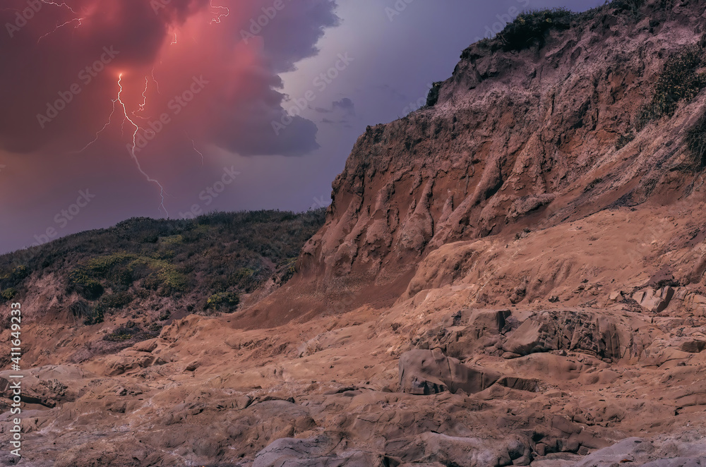 Thunderhead erupts with rain and lightning near Cambria on California coast with rugged sandstone cliffs and sand dune cover with ice plant nobody