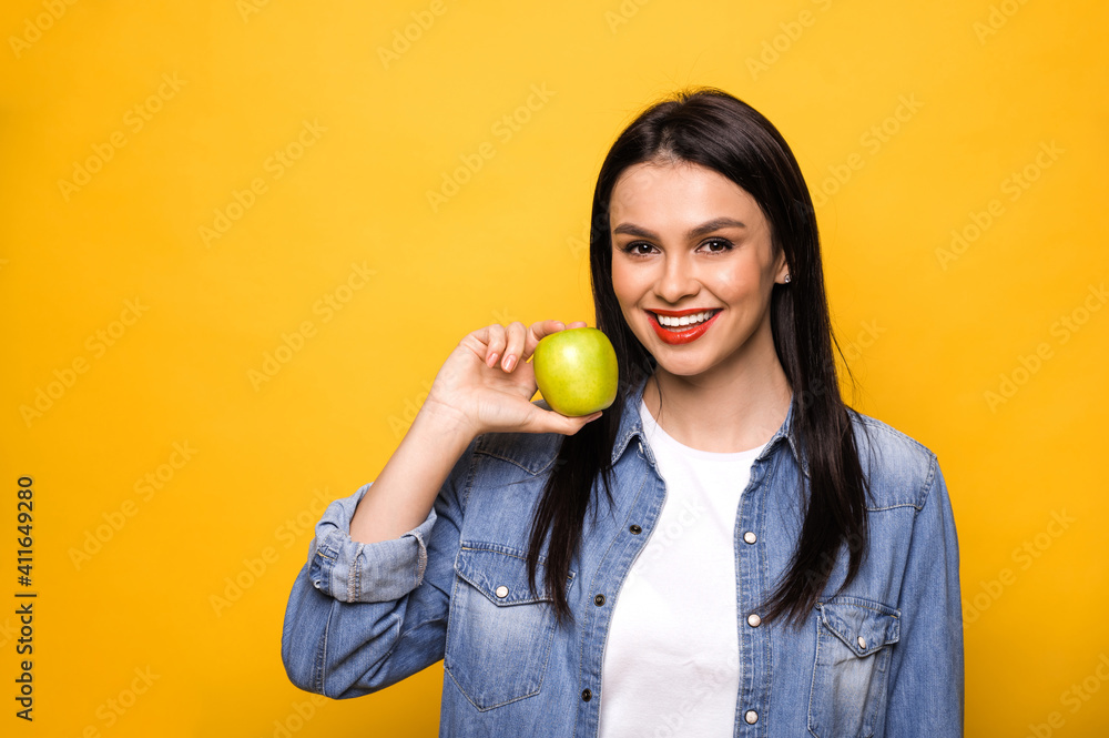 Young caucasian woman leads a healthy lifestyle. A girl stands on an isolated orange background, holds a fresh green apple, looks into the camera and smiles. Healthy food concept Young caucasian woman leads a healthy lifestyle. A girl stands on an isolated orange background, holds a fresh green apple, looks into the camera and smiles. Healthy food concept