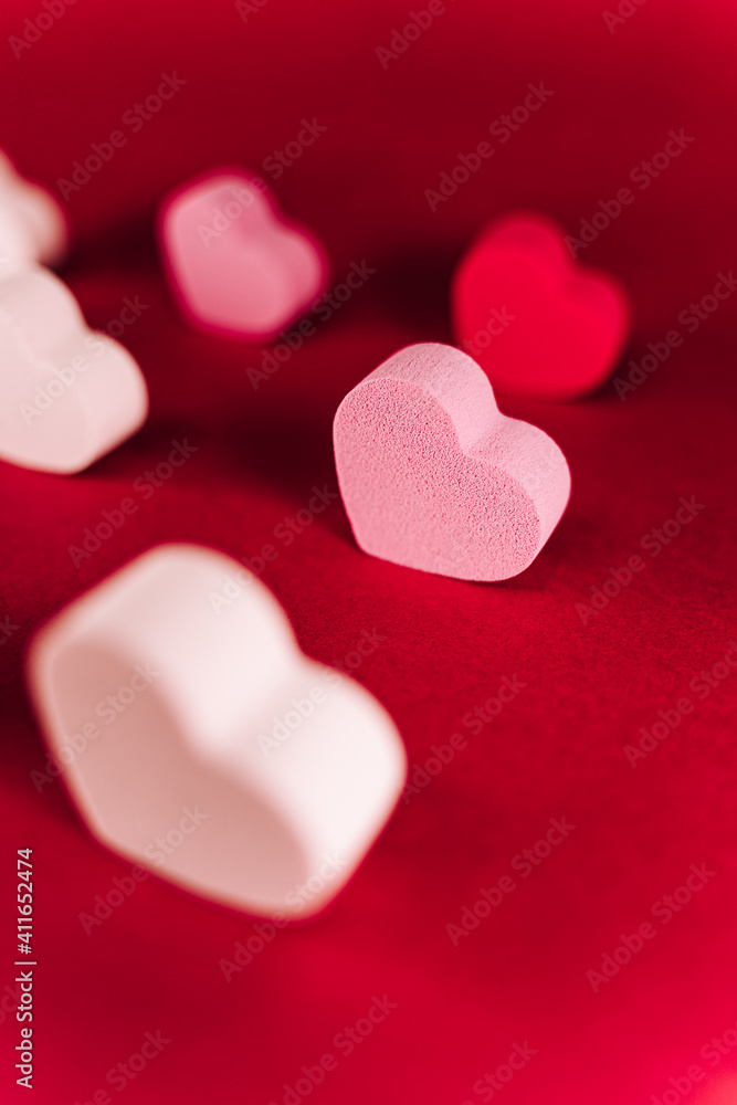 A little pink heart of sponge with with another hearts of sponge situated together on a red background. San Valentine's day backgrounds concept