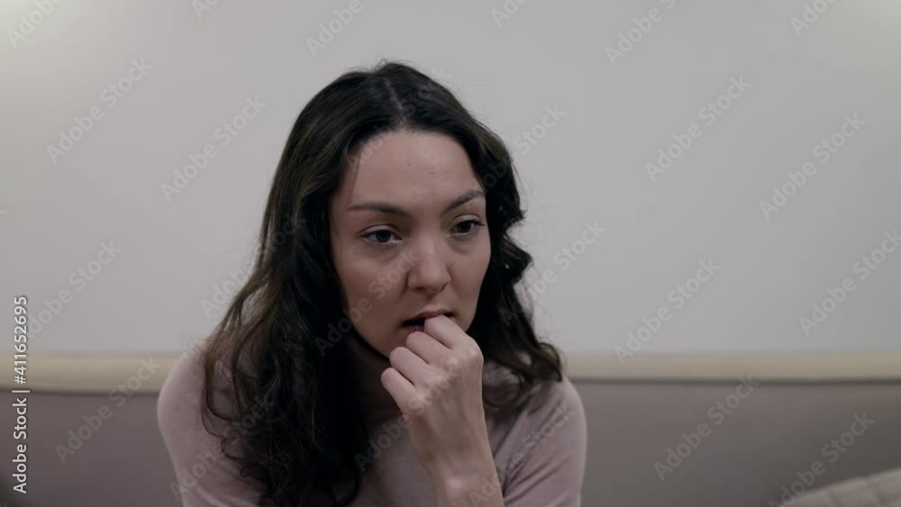 Portrait of a dark-haired woman pensive in a light jacket, sitting on a sofa in a bright room. Portrait of a dark-haired woman pensive in a light jacket, sitting on a sofa in a bright room.