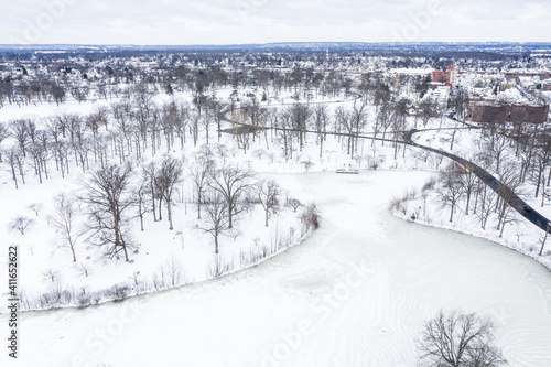 Aerial of a lake surrounded by snow-covered land and bare trees.