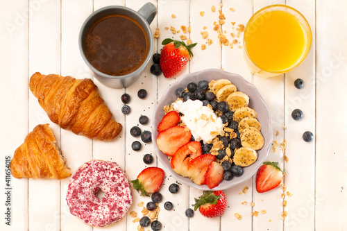 Fresh tasty breakfast with croissant, oat flakes, berries, donuts, coffee and orange jiuce on the white wooden table 