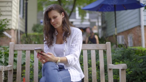 Caucasian Brunette Young Woman Sitting on Bench and Using Cell Phone photo