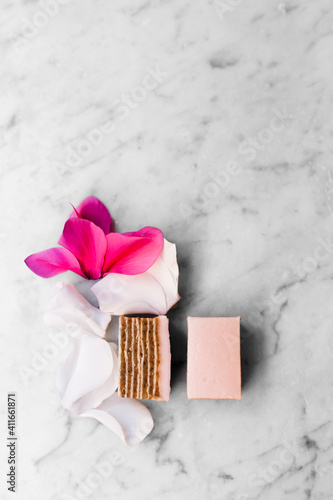 Pink cake and flower petals on white marble background.