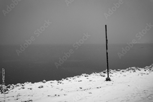 Single pole marker stuck in frozen ice and sand with calm lake and foggy sky in urban Chicago