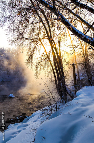 hristmas Lace.Winter landscape in pink tones with hoarfrost everywhere.Mostly calm winter river, surrounded by trees covered with hoarfrost and snow that falls on beautiful pink morning light.