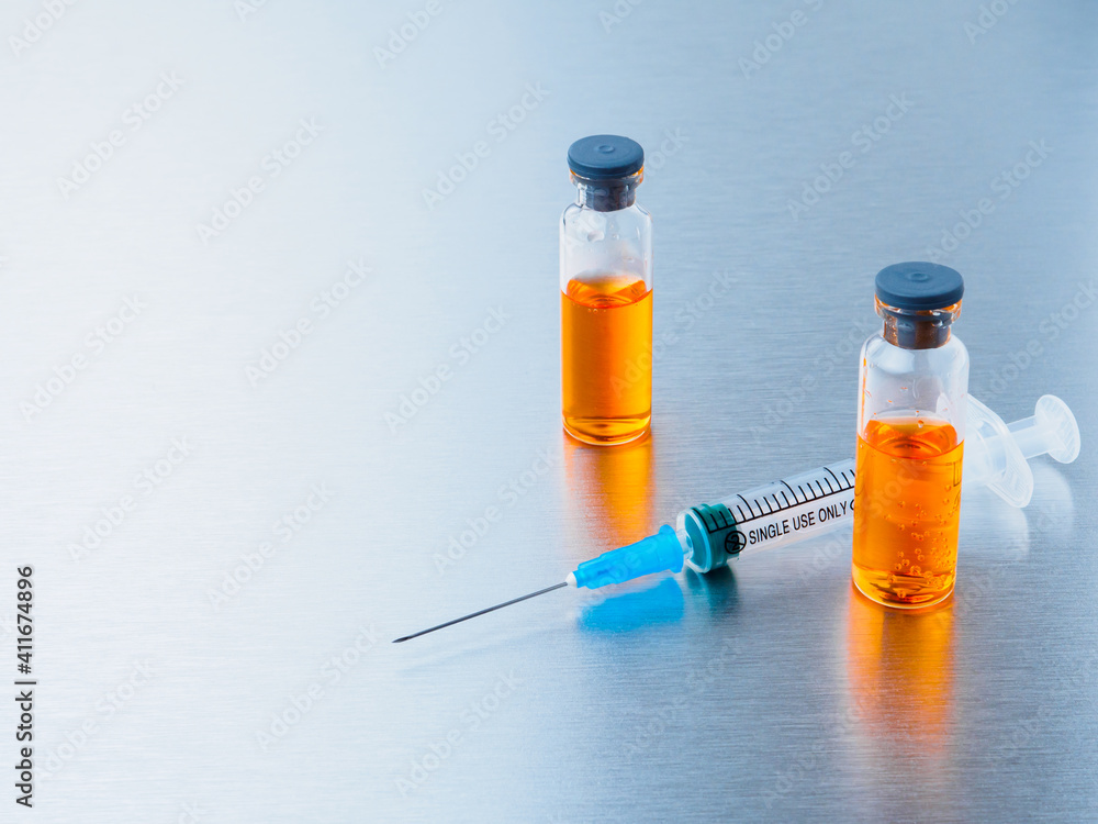 Selective focus. Syringe for injection and two ampoules of coronavirus vaccine on a silvery aluminum background. Covid-19 pandemic medical concept. Copy space. Selective focus. Syringe for injection and two ampoules of coronavirus vaccine on a silvery aluminum background. Covid-19 pandemic medical concept. Copy space.