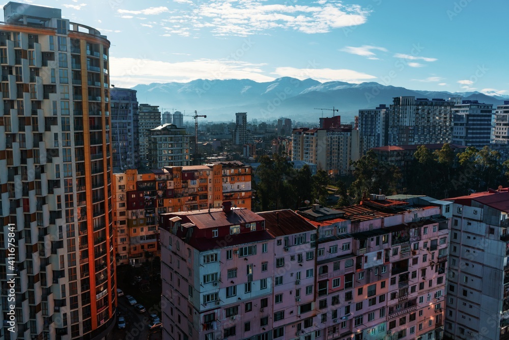 View of the city of Batumi from the window of a tall building. Panorama of old houses with balconies where clothes are dried. Slum together with skyscrapers against the background of blue mountains.