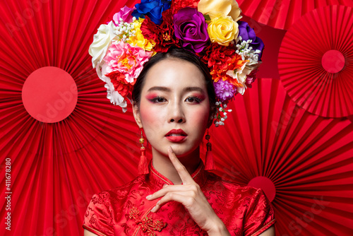 Gorgeous Asian woman in traditional Cheongsam dress with colorful make up and flower wreath on head in oriental style red fan background