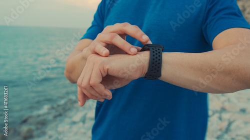 Sportsman wearing sportswear standing outdoors resting after a workout and using the smartwatch checking heart rate. Male taking a break after running workout. Healthy lifestyle concept. © Lifehdfilm
