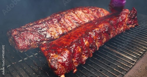 Chef basting barbecue sauce over baby back pork ribs on a wood pellet smoker grill photo