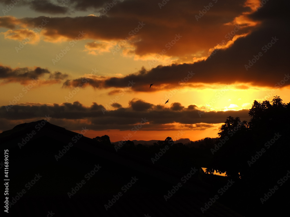Large image of a Stunning majestic gold sunset and beautiful shaped clouds with birds flying over mountains and trees in a small town in Brazil called Joanopolis located in the state of Sao Paulo
