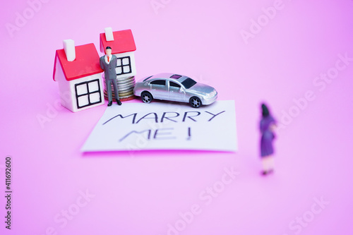 Marry me written on sticky note with miniature love couple in concept of married life  family planning  saving money  buying house and car