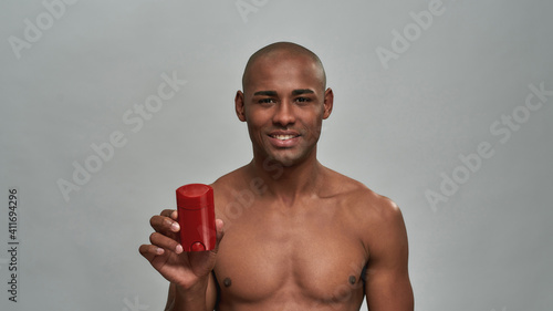 Cheerful man presenting a deodorant in a red packaging