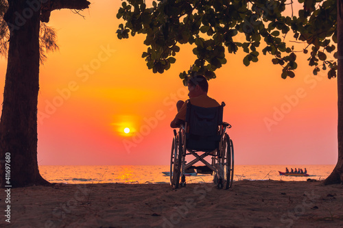 Asian special child on wheelchair on the sea beach with sunset on travel time in holiday family and learning about nature around the sea,Lifestyle in the education age kids,Happy disabled kid concept. © GAYSORN