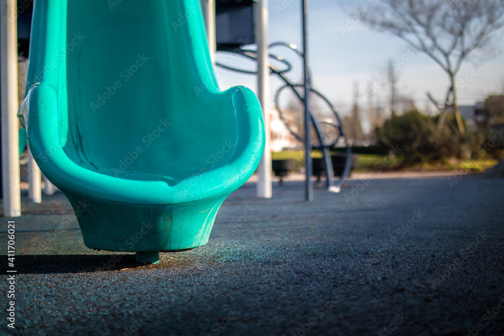 Partial slide in park playground, early mornings on a sunny day. Bright blue slide with rubberized dark blue shock absorbent surface. Selective focus with defocused playground and nature background. Partial slide in park playground, early mornings on a sunny day. Bright blue slide with rubberized dark blue shock absorbent surface. Selective focus with defocused playground and nature background.