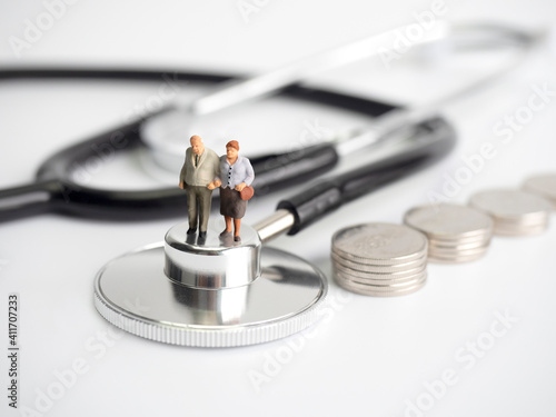 Miniature old people standing on medical stethoscope with coins stack on white background, Retirement planning, Emergency plan, Life insurance Concept.