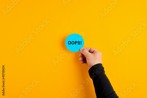 Male hand placing a blue badge with the word oops on yellow background. photo