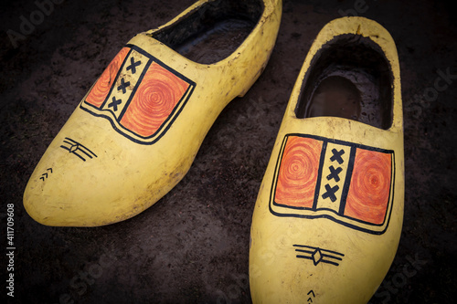 A slight downward and close up perspective of a pair of worn yellow and orange wooden shoes on a dark soil background