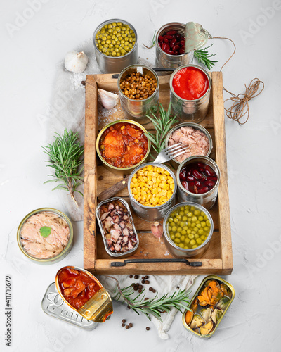 Various canned vegetables, fish and peas in aluminum cans on light gray background.